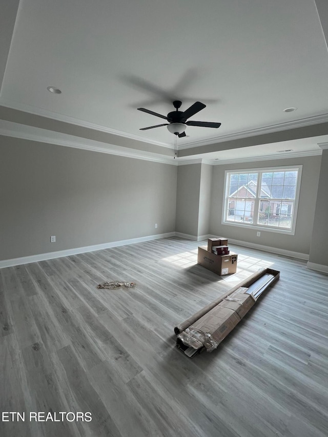 interior space with ceiling fan, a tray ceiling, hardwood / wood-style flooring, and crown molding