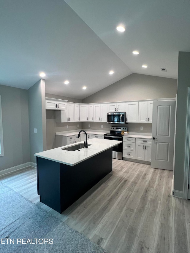 kitchen featuring appliances with stainless steel finishes, white cabinets, vaulted ceiling, light wood-type flooring, and sink