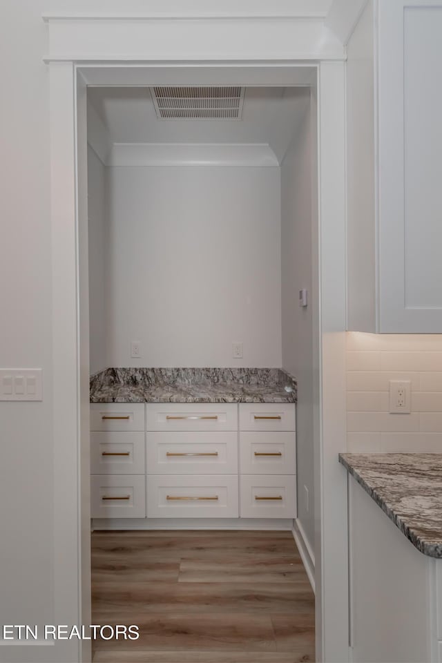 pantry featuring crown molding, light hardwood / wood-style floors, dark stone counters, and white cabinets