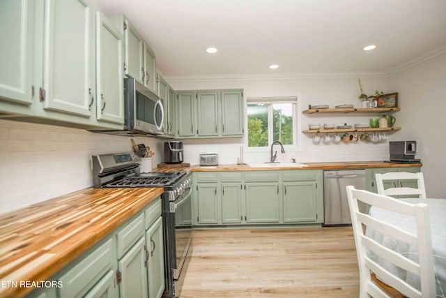 kitchen with backsplash, stainless steel appliances, green cabinetry, and light hardwood / wood-style flooring