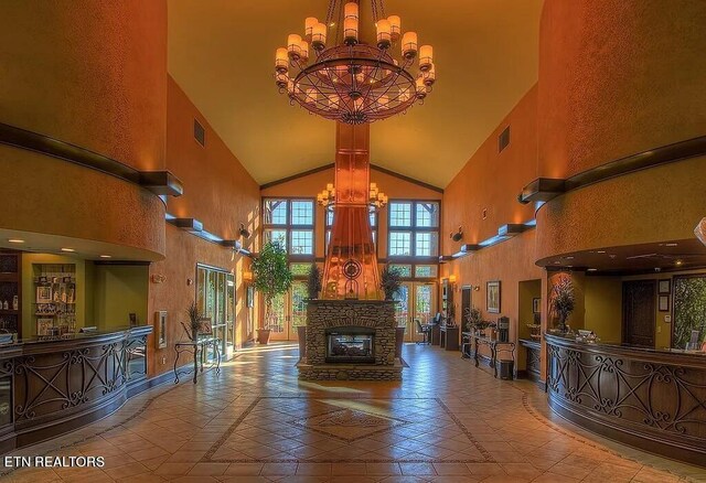 interior space with high vaulted ceiling, a fireplace, tile patterned floors, and an inviting chandelier