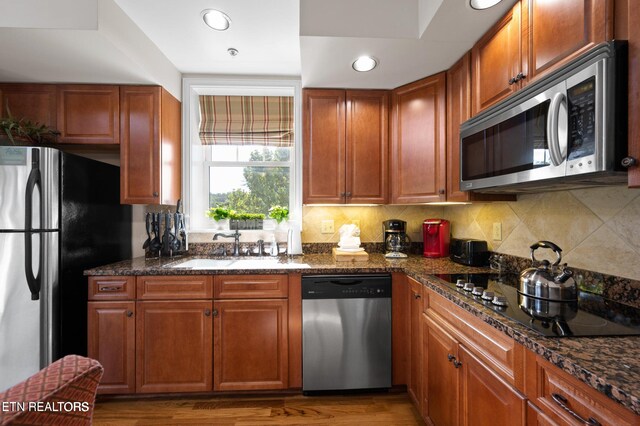 kitchen with decorative backsplash, stainless steel appliances, hardwood / wood-style flooring, and dark stone counters