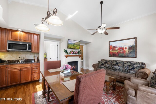 dining space with ceiling fan, high vaulted ceiling, dark wood-type flooring, and ornamental molding