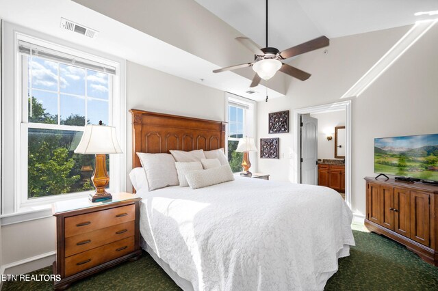 carpeted bedroom featuring ceiling fan, ensuite bathroom, multiple windows, and lofted ceiling