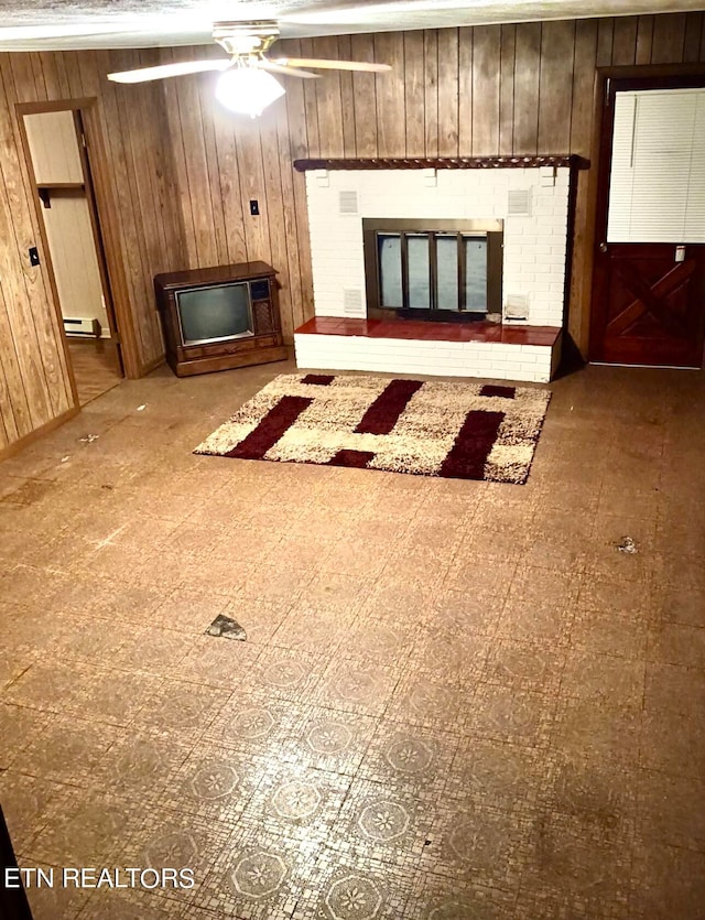 unfurnished living room with wood walls, ceiling fan, baseboard heating, and a fireplace