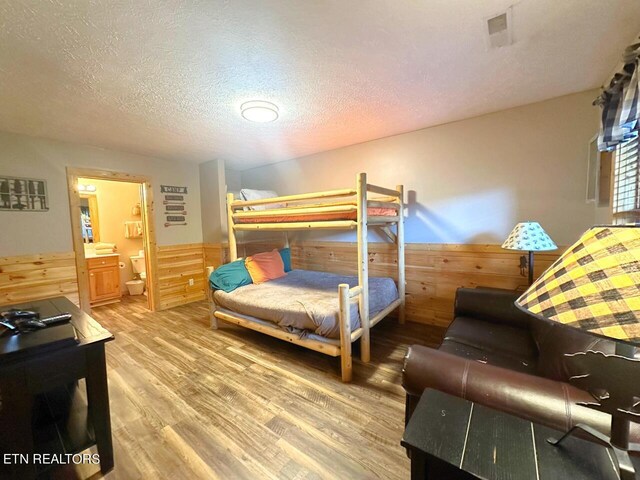 bedroom featuring connected bathroom, wood-type flooring, and a textured ceiling