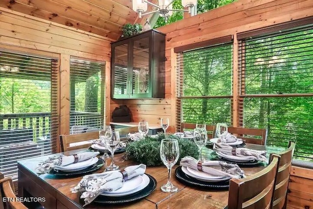 dining space with lofted ceiling, wooden walls, and a healthy amount of sunlight