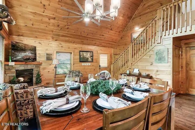 dining room with high vaulted ceiling, a stone fireplace, an inviting chandelier, wood-type flooring, and wooden walls