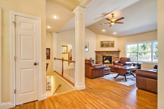 living room with ceiling fan, light hardwood / wood-style floors, a stone fireplace, vaulted ceiling, and ornate columns