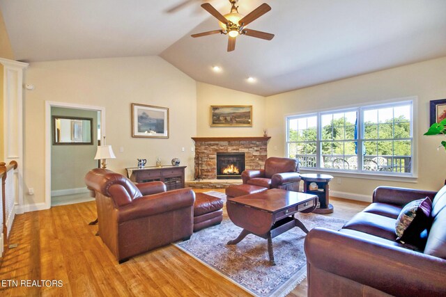 living room featuring lofted ceiling, a stone fireplace, ceiling fan, and light wood-type flooring