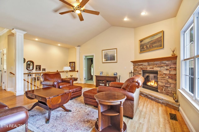 living room with lofted ceiling, a stone fireplace, light wood-type flooring, and ornate columns