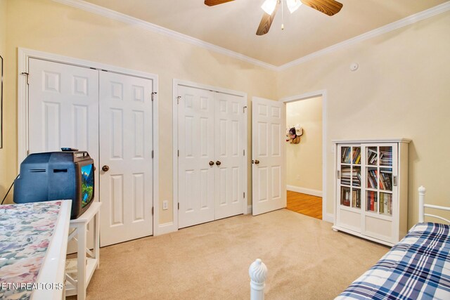 bedroom with crown molding, two closets, light colored carpet, and ceiling fan