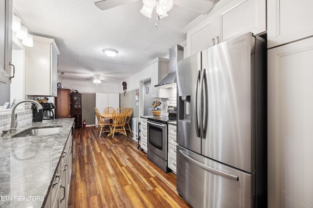 kitchen with sink, appliances with stainless steel finishes, hardwood / wood-style flooring, wall chimney exhaust hood, and ceiling fan