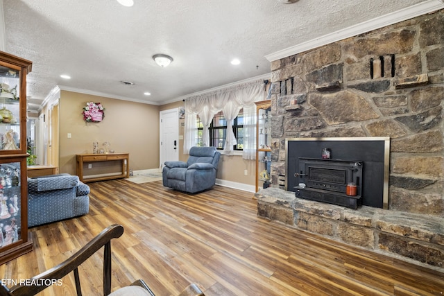 living room featuring a textured ceiling, crown molding, a stone fireplace, and wood-type flooring