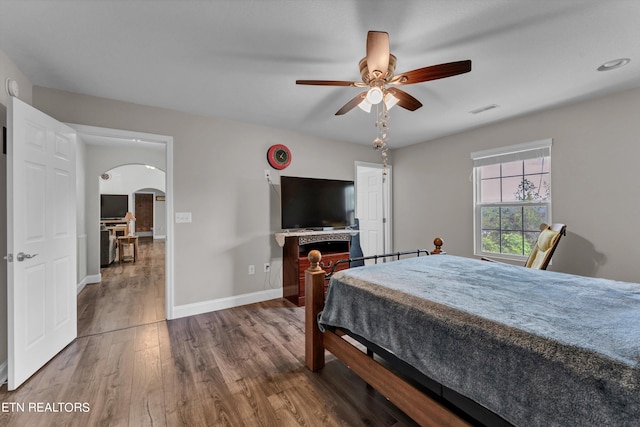 bedroom with ceiling fan, wood-type flooring, and a fireplace