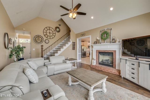 living room featuring ceiling fan, high vaulted ceiling, a brick fireplace, and hardwood / wood-style floors