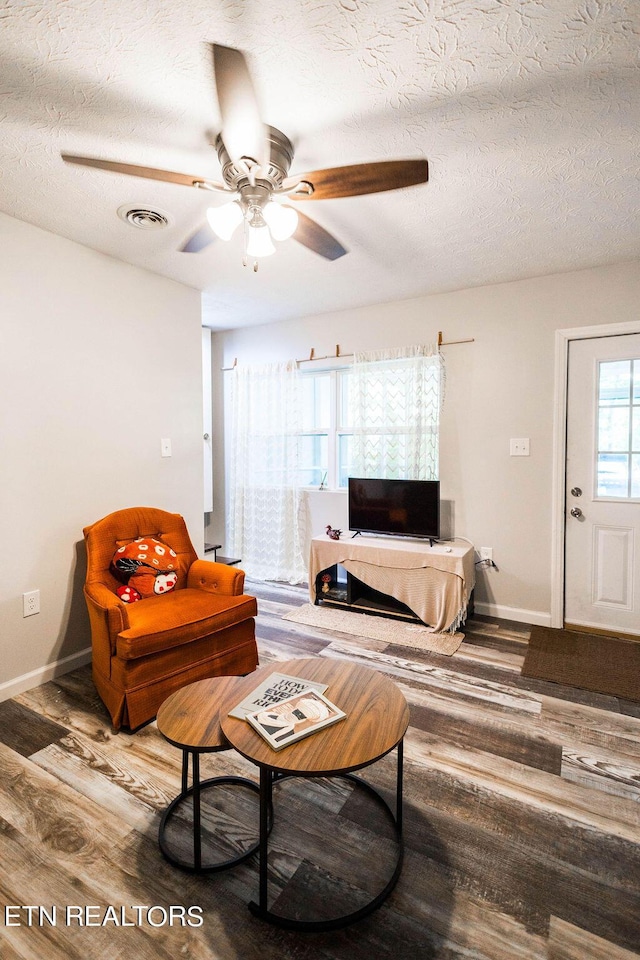 living room with a textured ceiling, ceiling fan, wood finished floors, visible vents, and baseboards