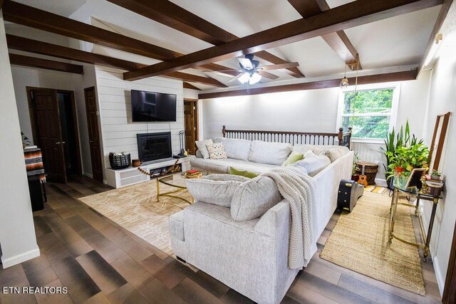 living room with ceiling fan, beam ceiling, dark wood-type flooring, and a large fireplace