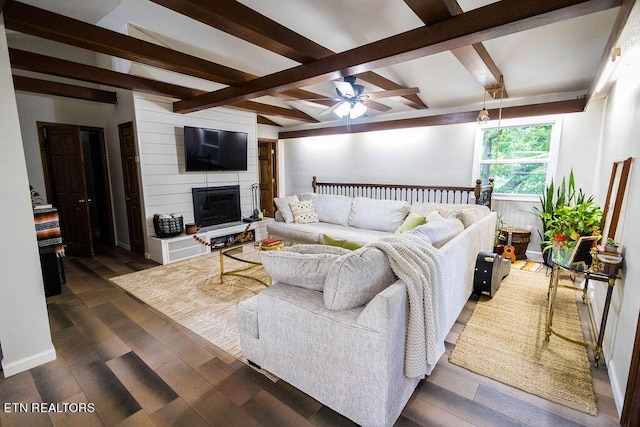 living room with a large fireplace, ceiling fan, dark wood-type flooring, and beamed ceiling