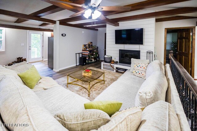 living room featuring ceiling fan, a large fireplace, beamed ceiling, and light wood-type flooring