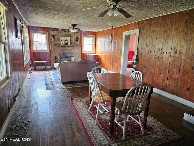 dining area with plenty of natural light, wooden walls, a large fireplace, and hardwood / wood-style flooring