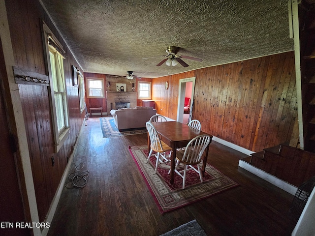 dining area featuring hardwood / wood-style floors, a fireplace, a textured ceiling, wooden walls, and ceiling fan