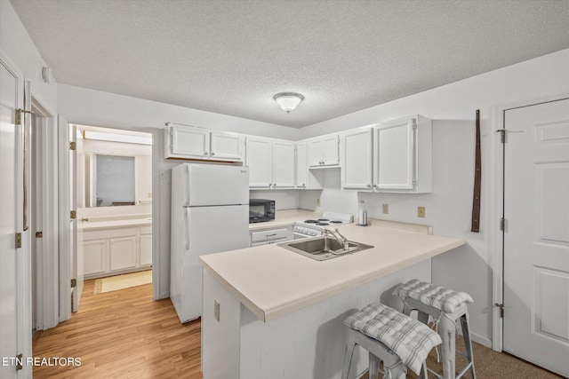 kitchen featuring a peninsula, light countertops, freestanding refrigerator, and white cabinets