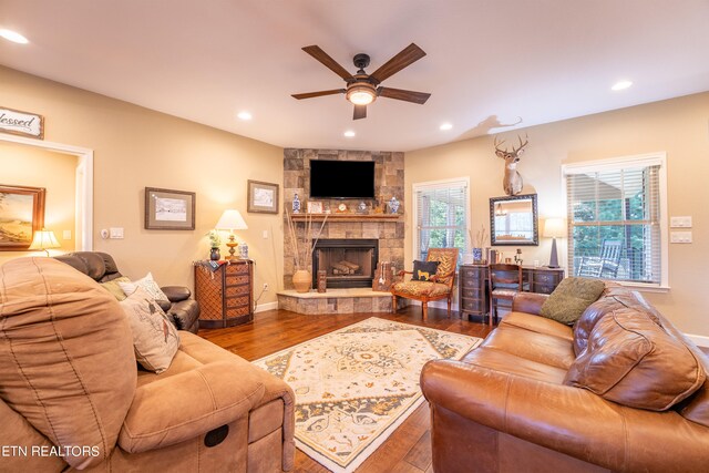 living room with ceiling fan, a stone fireplace, and hardwood / wood-style floors