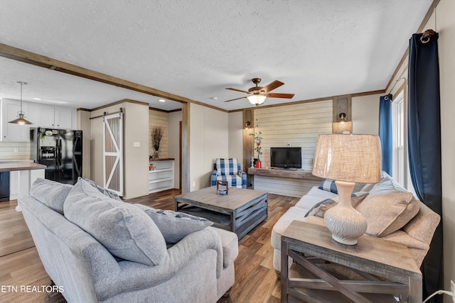 living room featuring hardwood / wood-style floors, a barn door, a textured ceiling, and ceiling fan