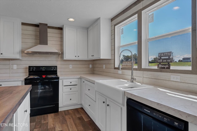 kitchen featuring wall chimney exhaust hood, plenty of natural light, black appliances, white cabinets, and dark wood-type flooring