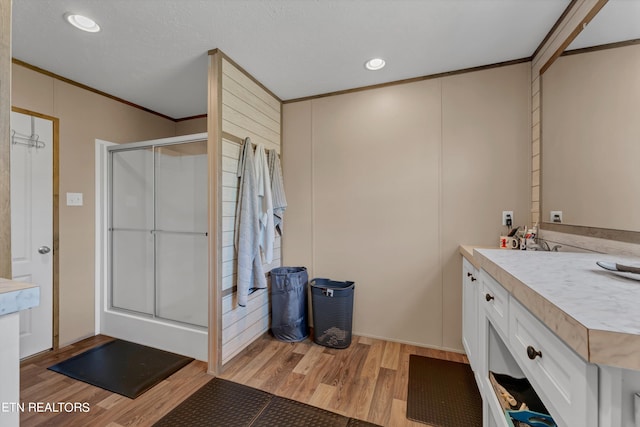 bathroom featuring a shower with door, hardwood / wood-style flooring, crown molding, and vanity