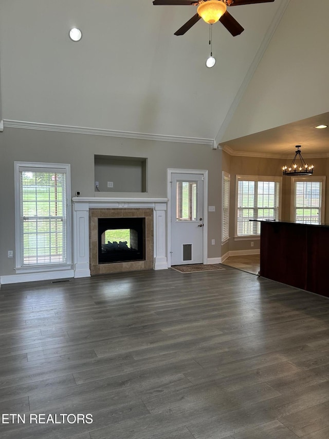 unfurnished living room with crown molding, baseboards, high vaulted ceiling, a tile fireplace, and ceiling fan with notable chandelier