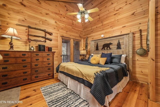 bedroom featuring light wood-type flooring, wood walls, a high ceiling, and a ceiling fan