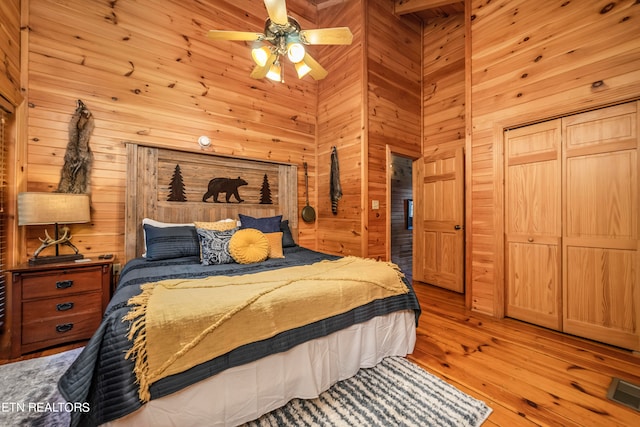 bedroom featuring ceiling fan, wooden walls, a high ceiling, a closet, and light hardwood / wood-style floors