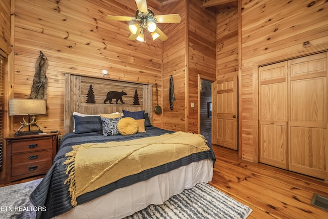 bedroom with ceiling fan, a high ceiling, wood walls, visible vents, and light wood-type flooring