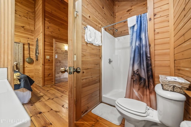 bathroom with a stall shower, wood finished floors, toilet, and wooden walls