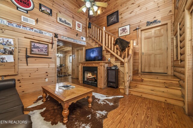 living room with hardwood / wood-style floors, ceiling fan with notable chandelier, and wooden walls