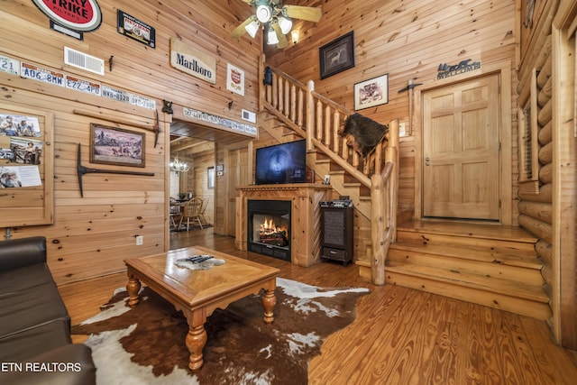 living room featuring wood finished floors, a towering ceiling, stairs, log walls, and a glass covered fireplace