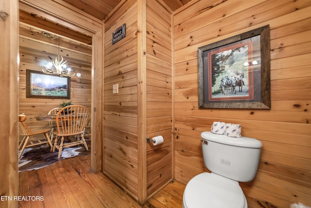 bathroom with an inviting chandelier, wood finished floors, toilet, and wooden walls