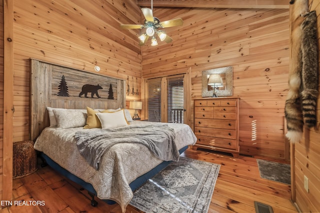 bedroom with a towering ceiling, wood walls, visible vents, and hardwood / wood-style floors