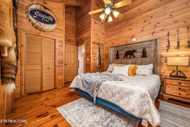 bedroom featuring a high ceiling, wooden walls, wood-type flooring, a closet, and ceiling fan