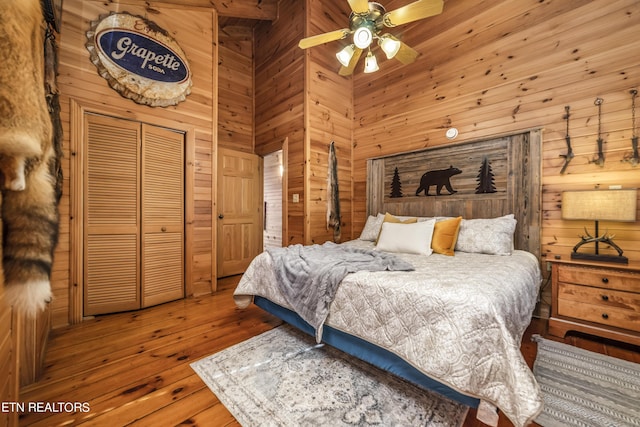 bedroom with a closet, a towering ceiling, hardwood / wood-style flooring, and wooden walls