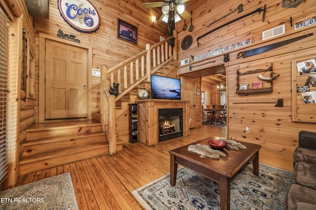 living room featuring visible vents, a glass covered fireplace, a towering ceiling, wood-type flooring, and stairs