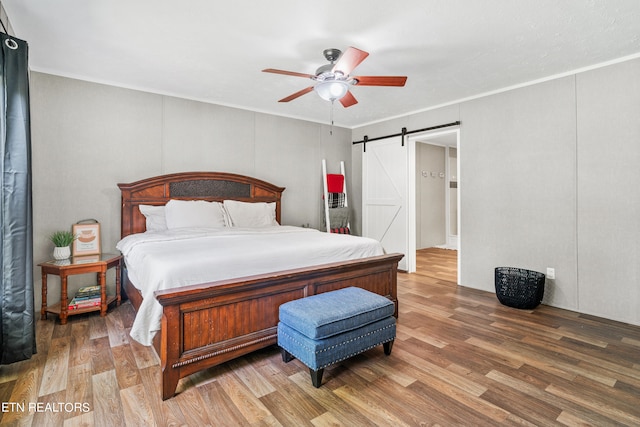 bedroom featuring ceiling fan, a barn door, and hardwood / wood-style flooring