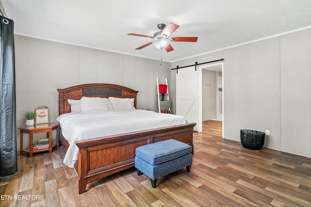 bedroom featuring ceiling fan, a barn door, wood finished floors, and crown molding