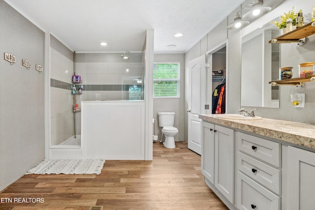 full bath featuring toilet, wood finished floors, a spacious closet, vanity, and a walk in shower