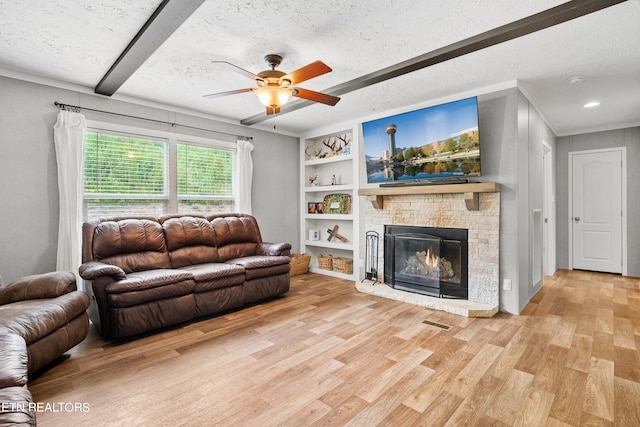 living room featuring ceiling fan, light wood-type flooring, a stone fireplace, a textured ceiling, and beamed ceiling