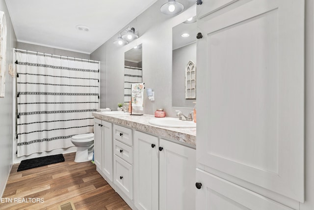 full bath featuring toilet, double vanity, a sink, and wood finished floors