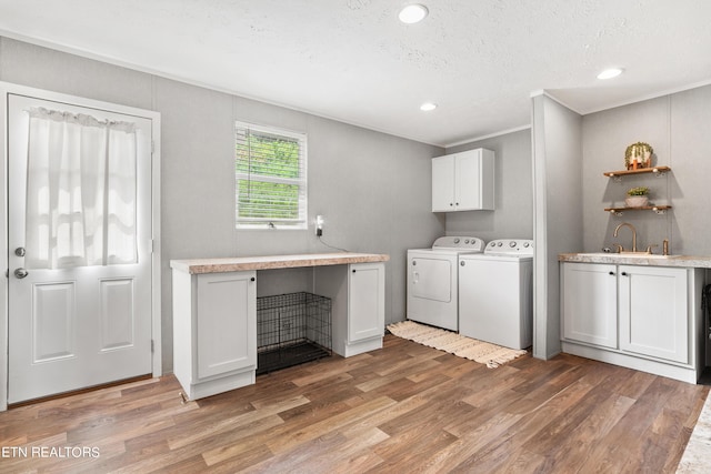 washroom with light wood finished floors, cabinet space, a sink, a textured ceiling, and separate washer and dryer