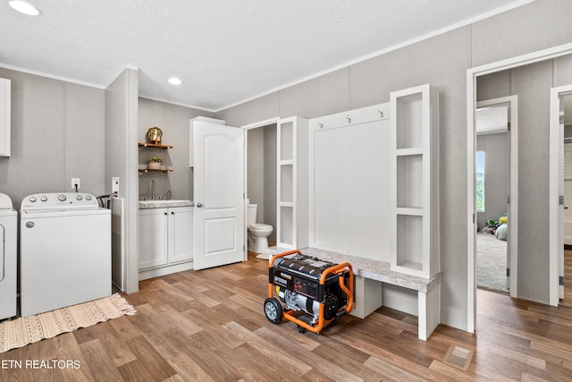 laundry area featuring a decorative wall, ornamental molding, cabinet space, light wood finished floors, and washer and clothes dryer